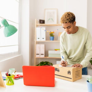 Hispanic latin young seller man preparing second hand package before sending to buyer - Young male seller writing address on box